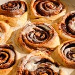 Close-up of freshly baked vegan protein cinnamon rolls topped with a silky vanilla coconut cream icing. The soft, fluffy cinnamon rolls feature thick cinnamon sugar swirls with golden-brown edges, while the warm icing melts into every layer, creating a rich, gooey texture perfect for breakfast or dessert.