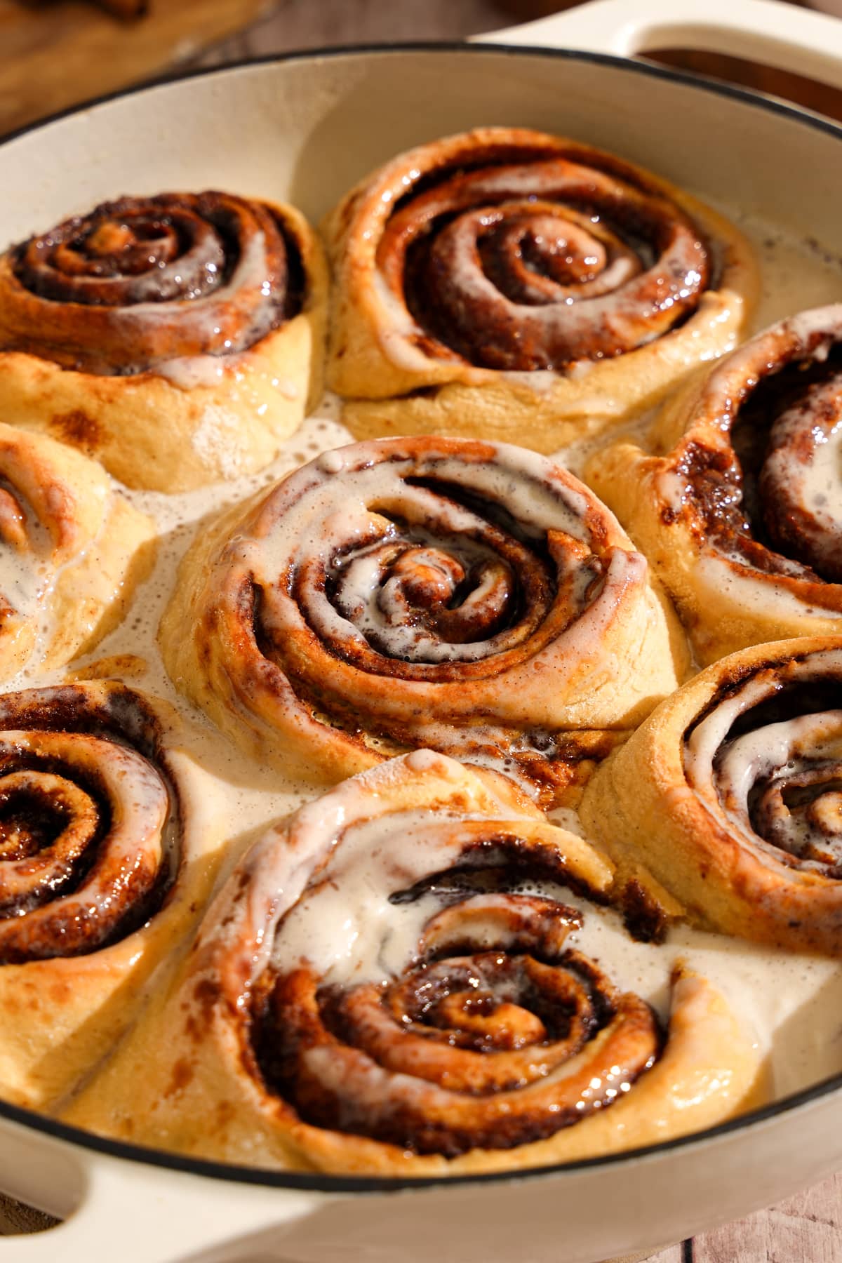 Close-up of soft and fluffy vegan protein cinnamon rolls baked in a cream-colored pan and covered with a creamy vanilla glaze. The warm cinnamon rolls have gooey cinnamon swirls and are coated in rich icing, making them the perfect cozy breakfast or brunch treat.