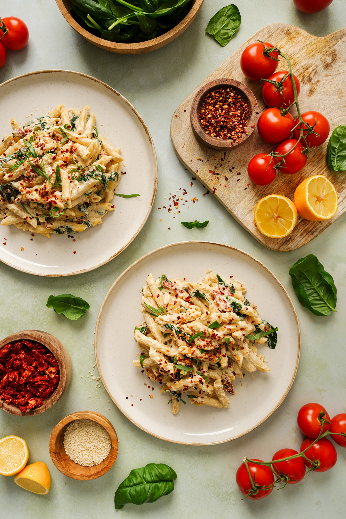 two plates of the tahini pasta with fresh ingredients all around it