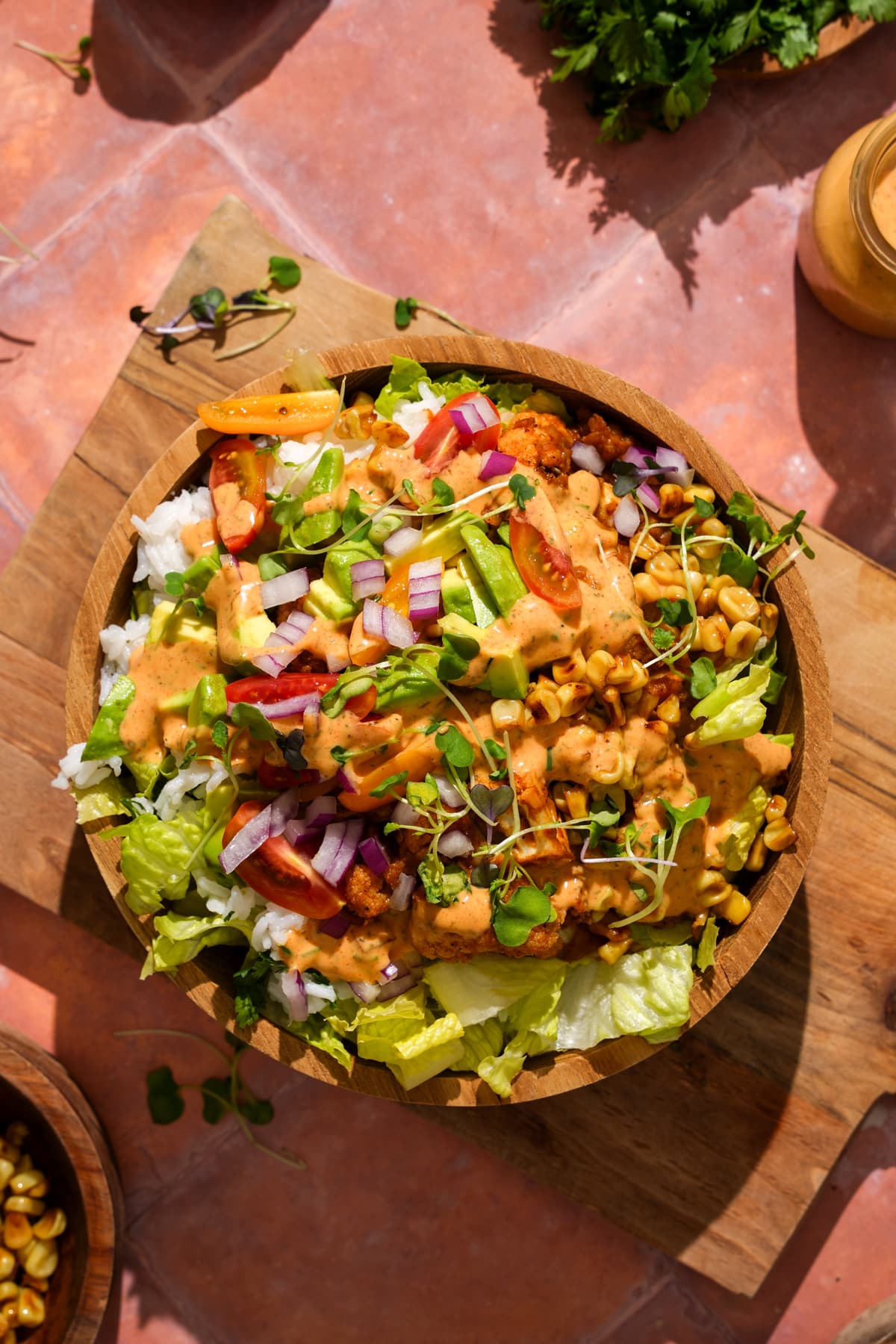Overhead view of a vegan cauliflower taco salad in a wooden bowl with romaine lettuce, cilantro lime rice, taco-seasoned cauliflower and red lentils, roasted corn, avocado, cherry tomatoes, red onion, microgreens, and creamy chipotle ranch dressing.