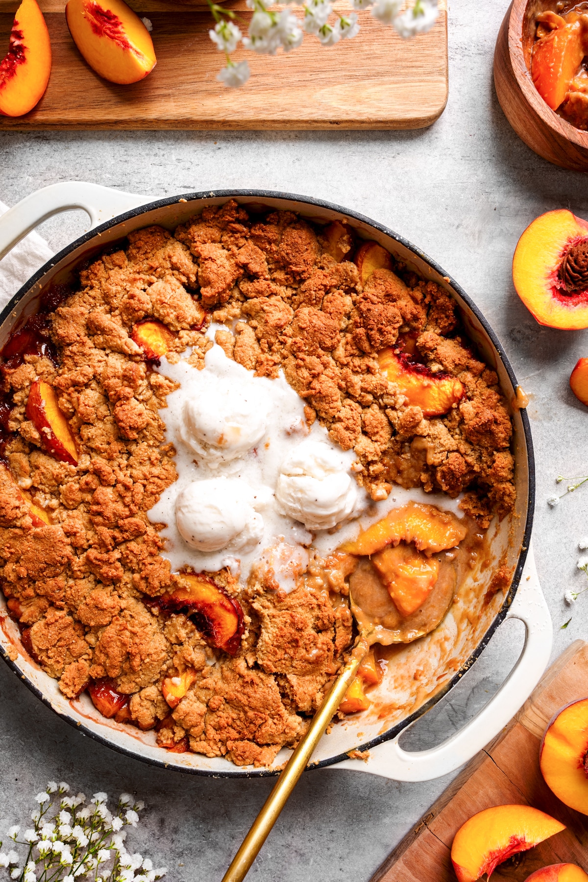 the peach cobbler in a skillet with a spoon scooping some out and vanilla ice cream melting on top