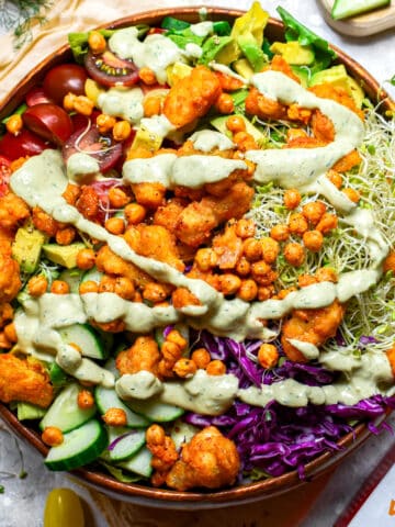 Close-up of vegan buffalo cauliflower salad with crispy chickpeas, avocado, cucumber, cherry tomatoes, sprouts, purple cabbage, and creamy dairy-free ranch dressing