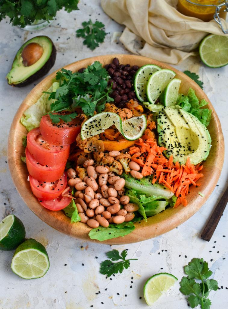 cauliflower taco salad overhead shot featuring avocado, pinto beans, tomato, romaine, black beans, cauliflower, cilantro