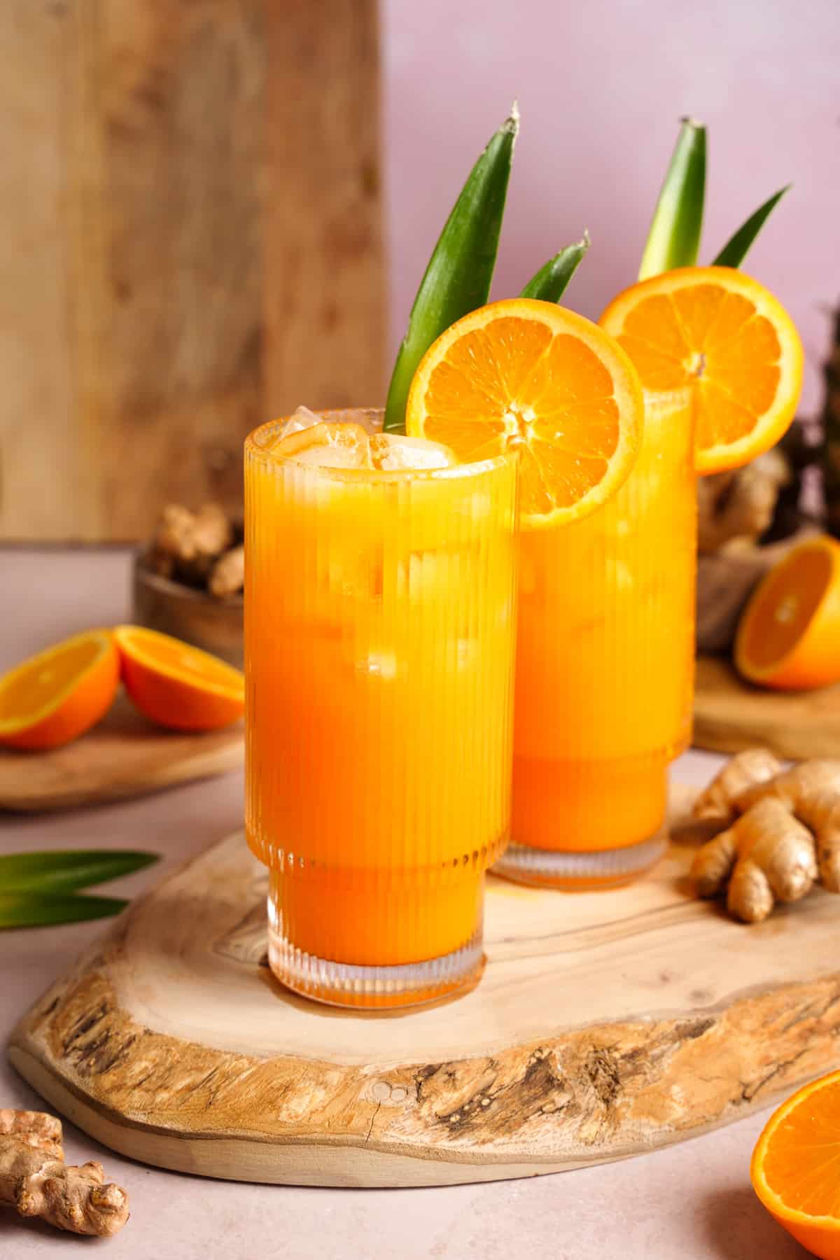 two glasses of the turmeric ginger glow juice garnished with orange slices and pineapple leaves