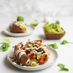 plates with the vegan taco stuffed sweet potatoes and a bowl of guacamole