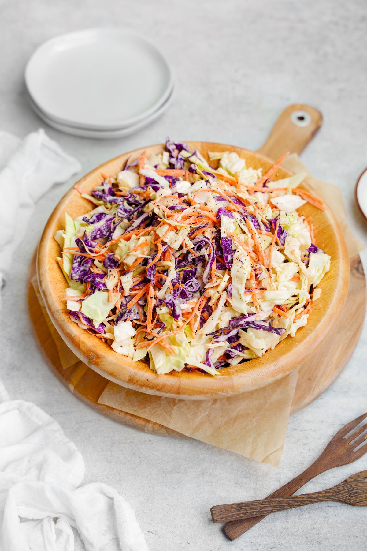 the healthy vegan coleslaw in a wood salad bowl with plats and forks around it