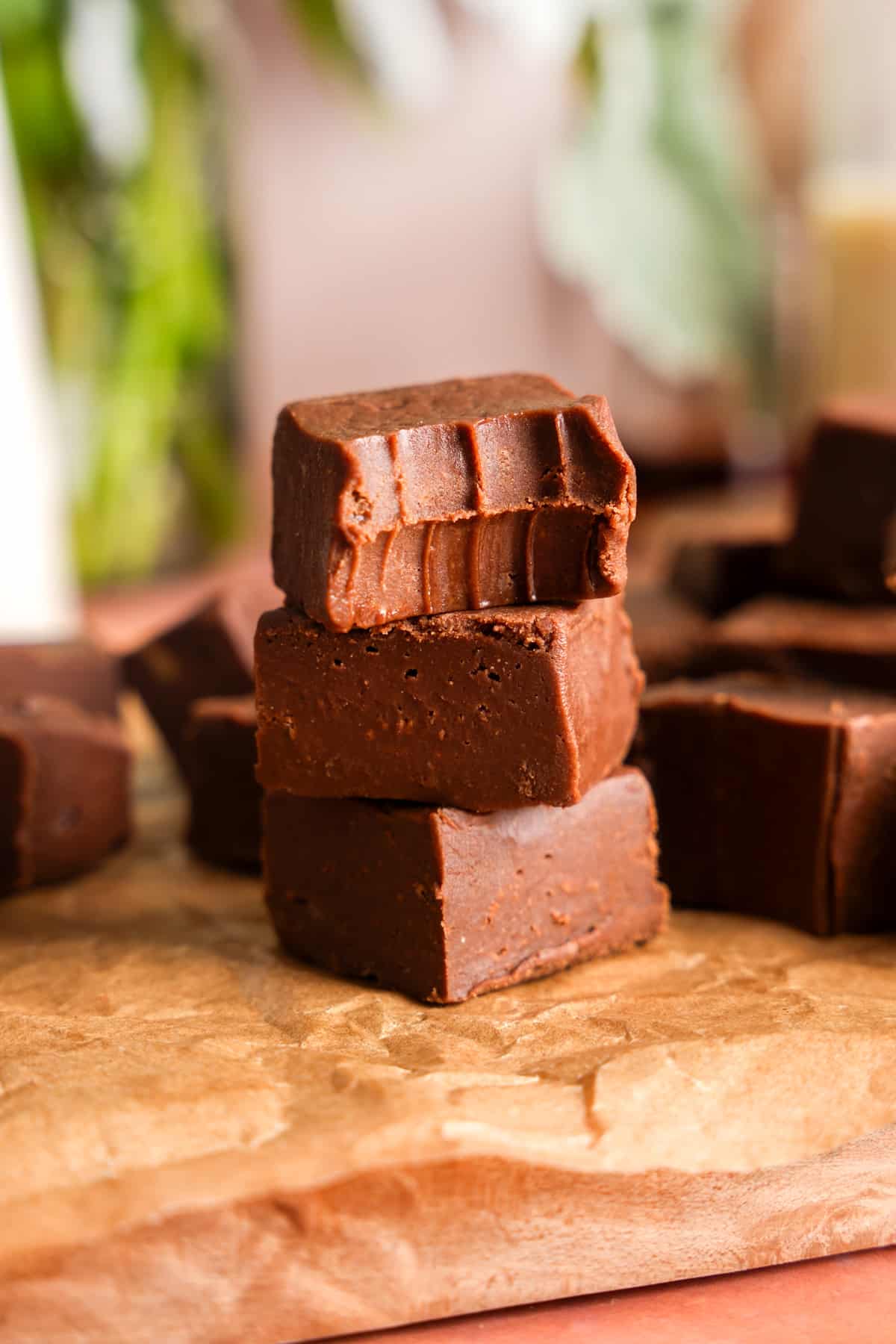 Stack of rich vegan chocolate protein fudge squares on parchment paper, with a smooth, dense texture and glossy finish, made with plant-based protein and refined sugar-free ingredients.