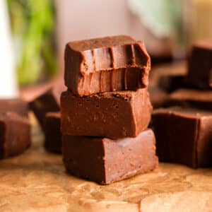 Stacked squares of creamy vegan chocolate protein fudge on parchment paper, showing a smooth, rich texture with a softly blurred kitchen background.