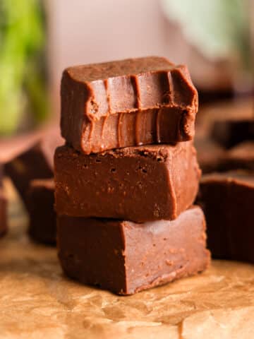 Stacked squares of creamy vegan chocolate protein fudge on parchment paper, showing a smooth, rich texture with a softly blurred kitchen background.