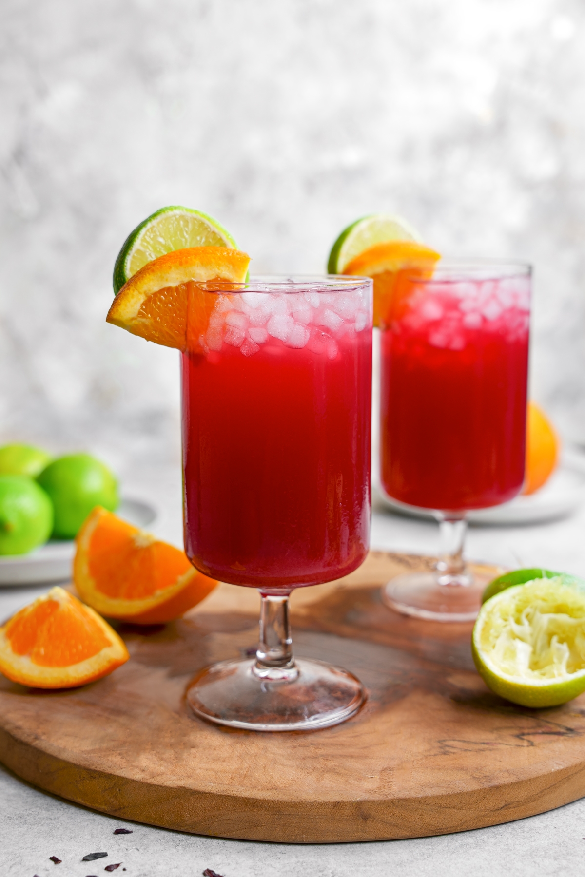 the hibiscus margarita mocktail in glasses with oranges and limes surrounding them