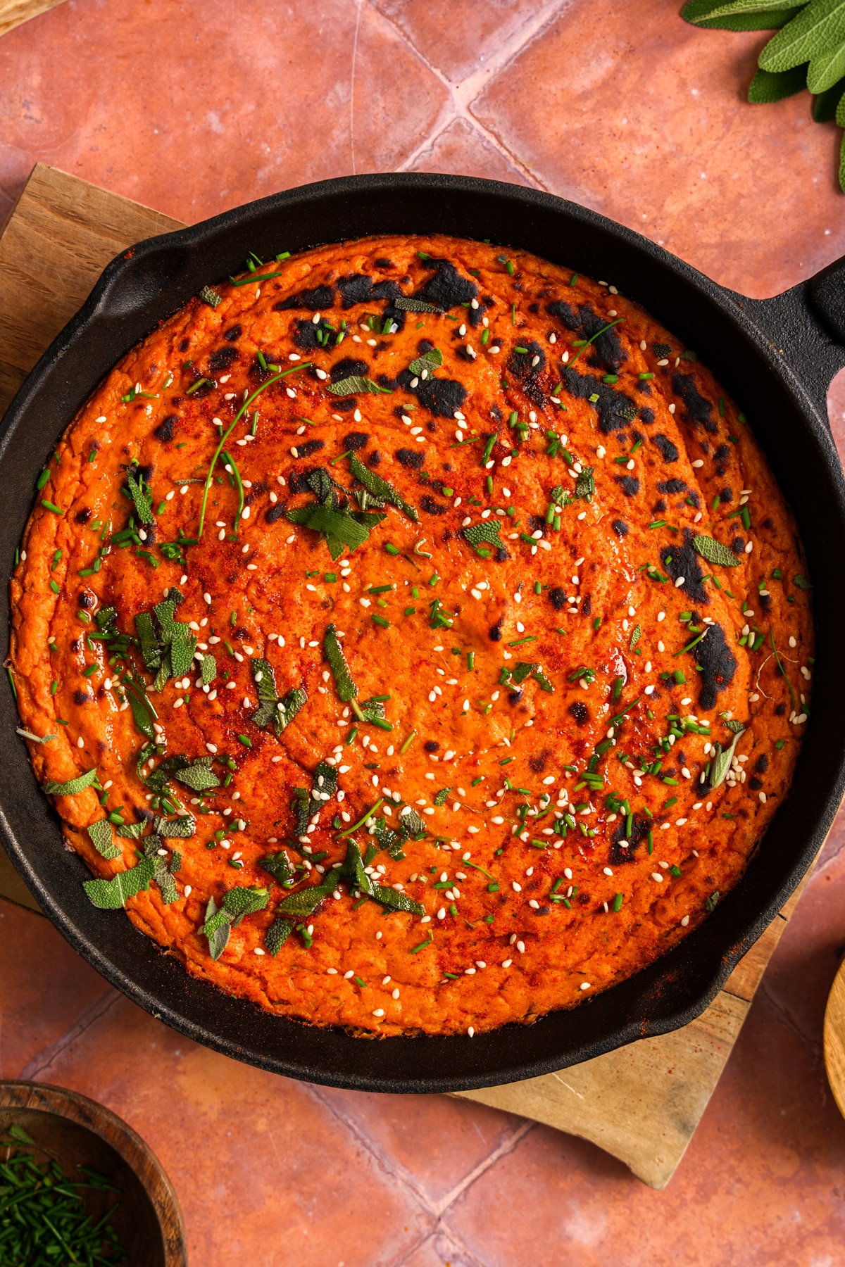 Overhead view of creamy vegan butternut squash dip baked in a cast iron skillet and topped with fresh herbs, sesame seeds, and a sprinkle of seasoning.