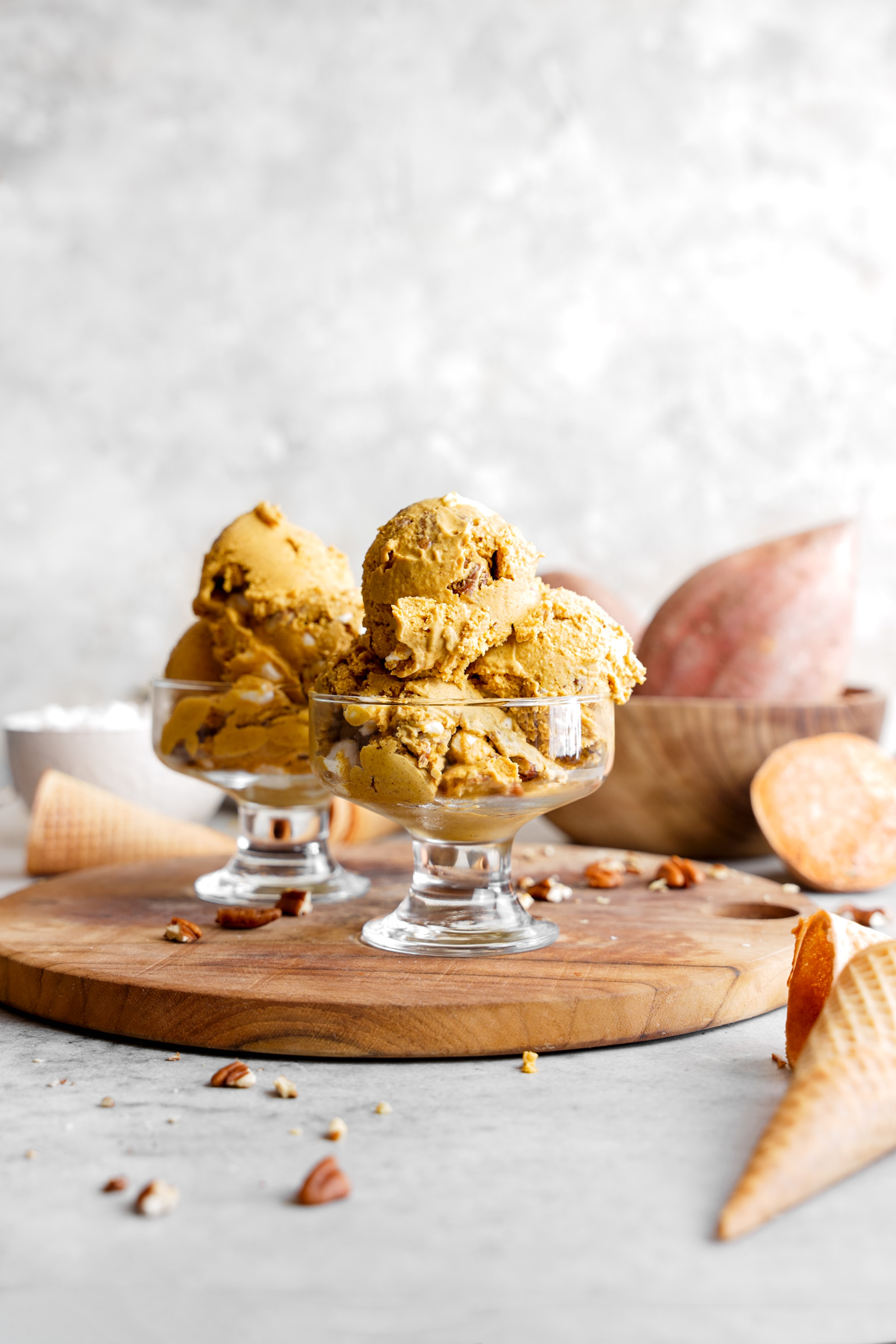the sweet potato ice cream scooped into ice cream glasses with sweet potatoes pecans and marshmallows surrounding it