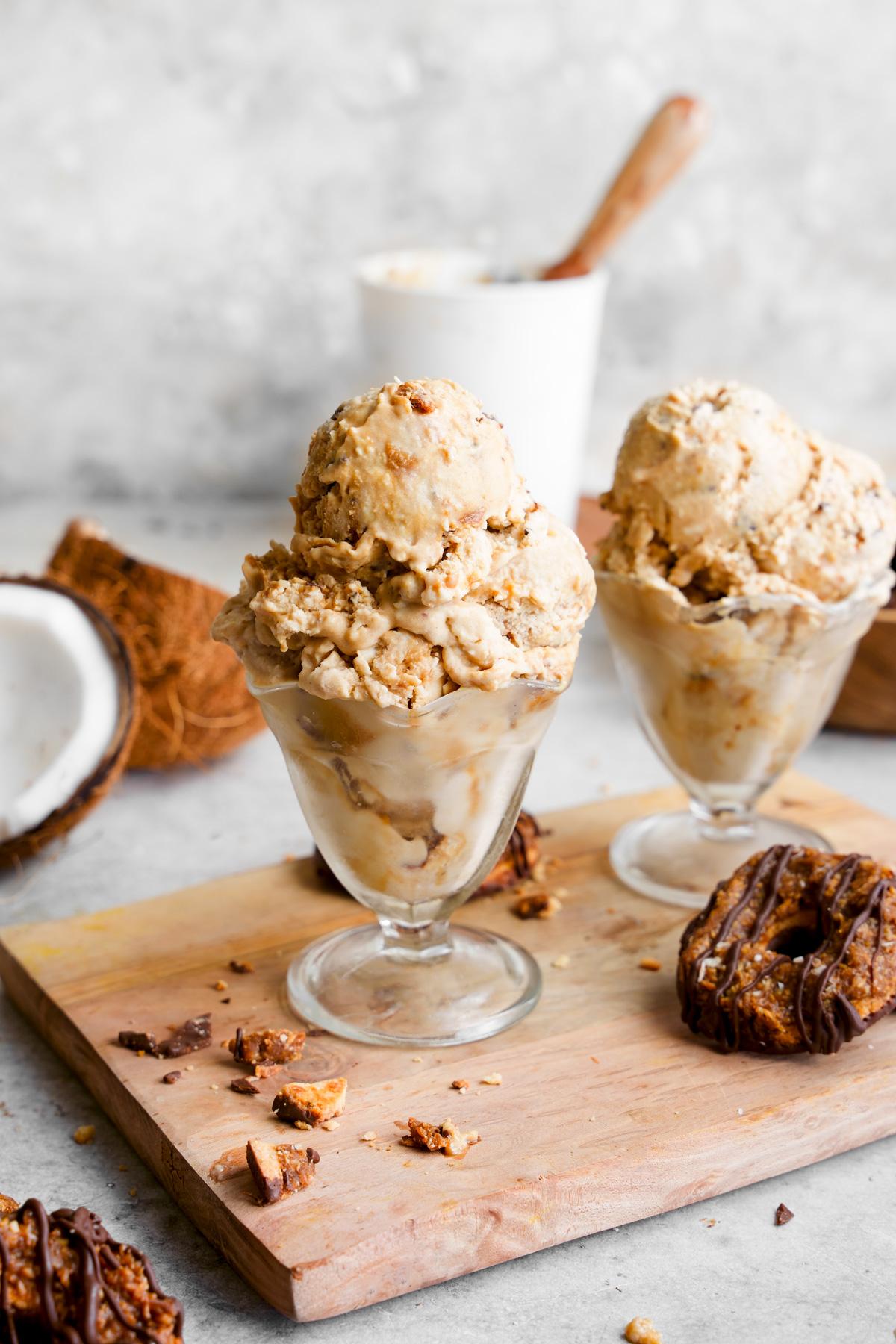 the samoa ice cream scooped into ice cream containers with fresh baked samoa cookies around it