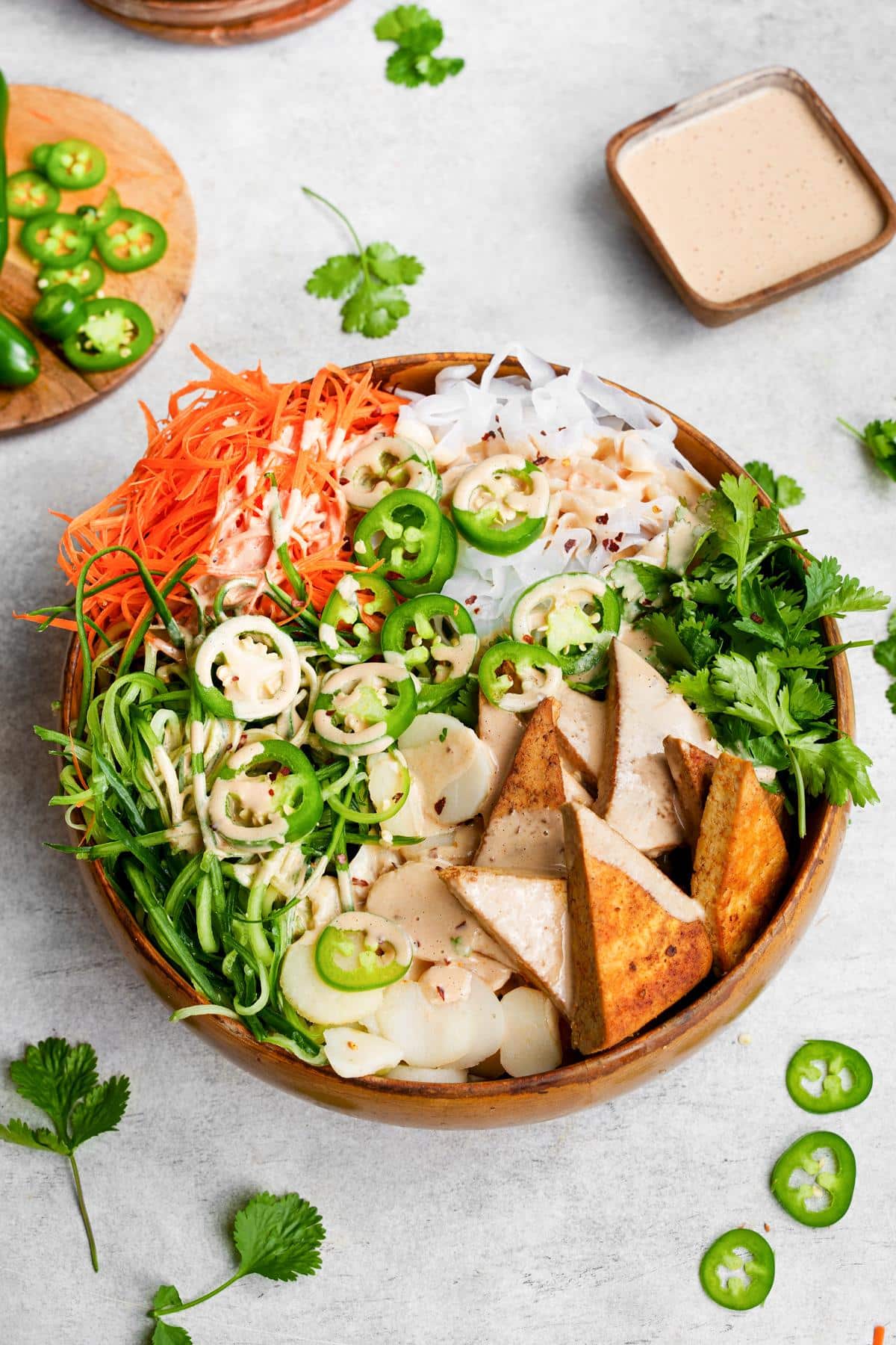 the banh mi noodles in a bowl with the creamy sriracha dressing and fresh jalapeños