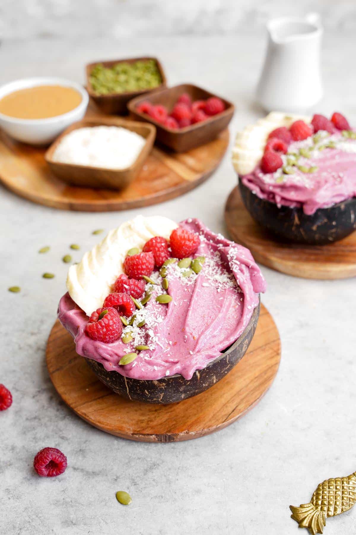 two coconut bowls filled with the raspberry smoothie bowl and toppings