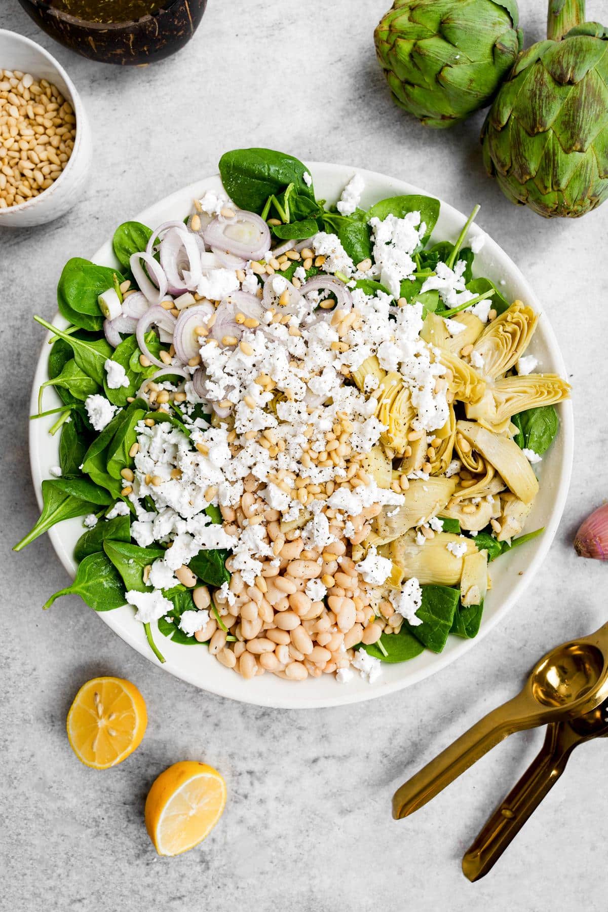 looking down at the spinach artichoke salad with fresh artichokes and lemons around thee bowl