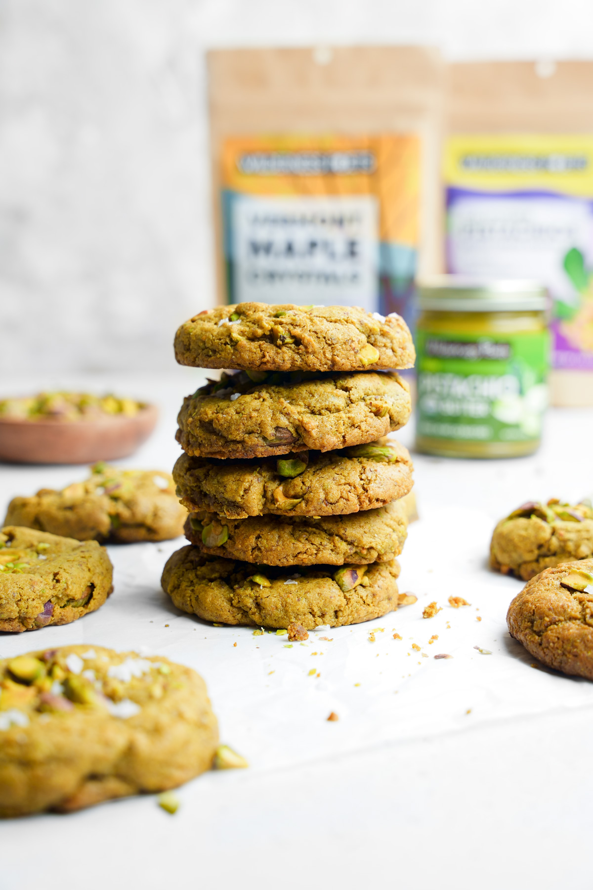 the vegan pistachio cookies stacked on top of each other with the wilderness poets products in the back
