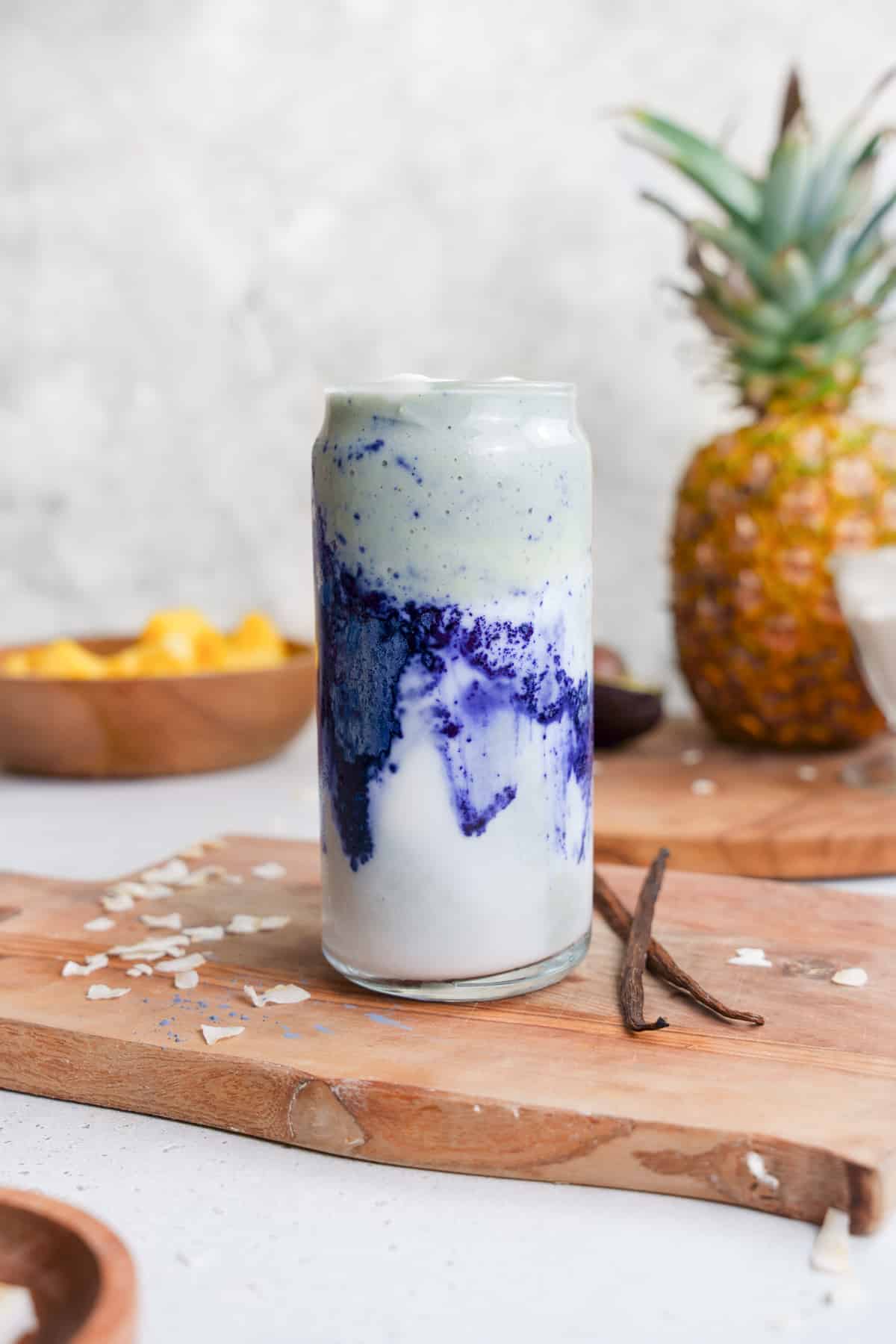 the blue magic smoothie with vanilla bean next to it and the fresh smoothie ingredients behind it