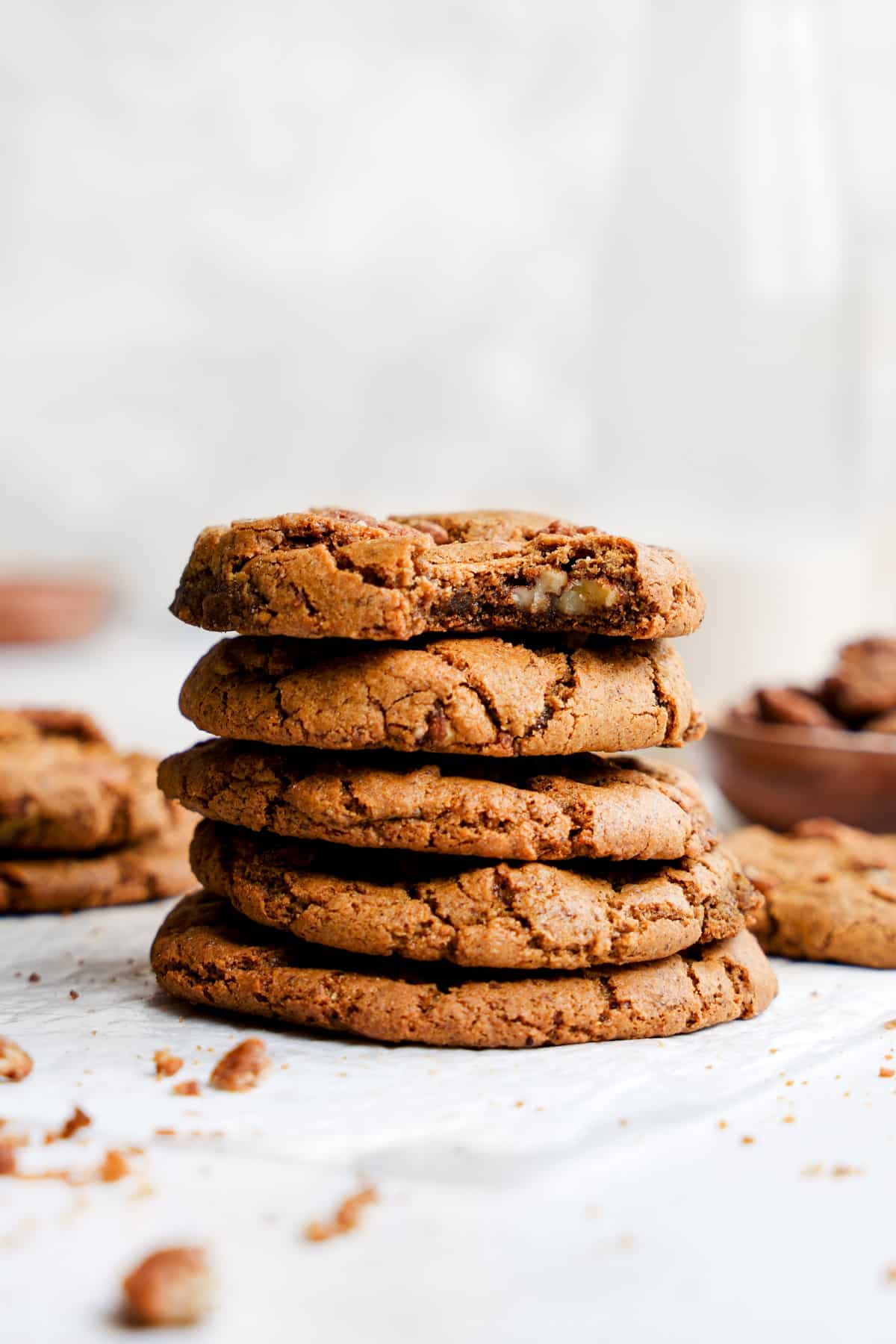 the vegan pecan cookies stacked on top of each other with a bite taken out of the top one to show the soft chewy center