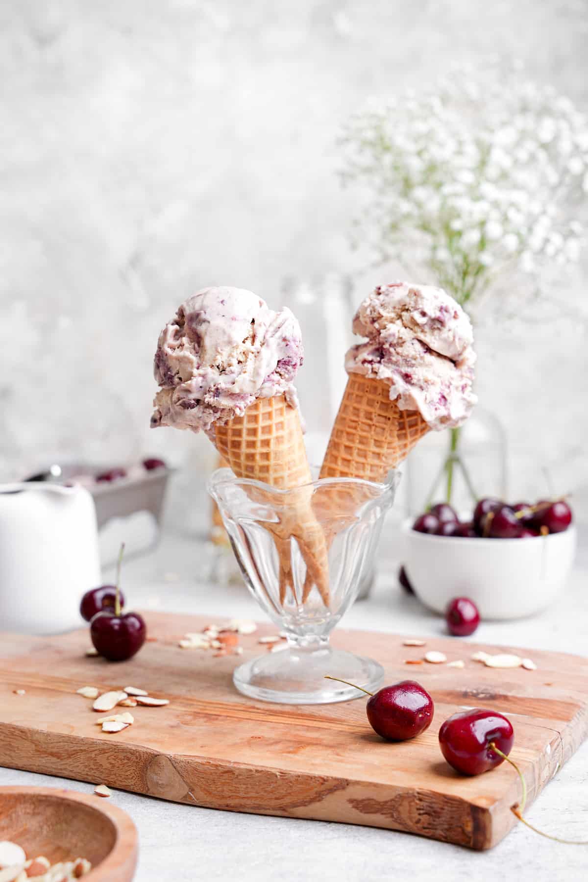 the almond cherry ice cream in ice cream cones with fresh cherries and almonds all around