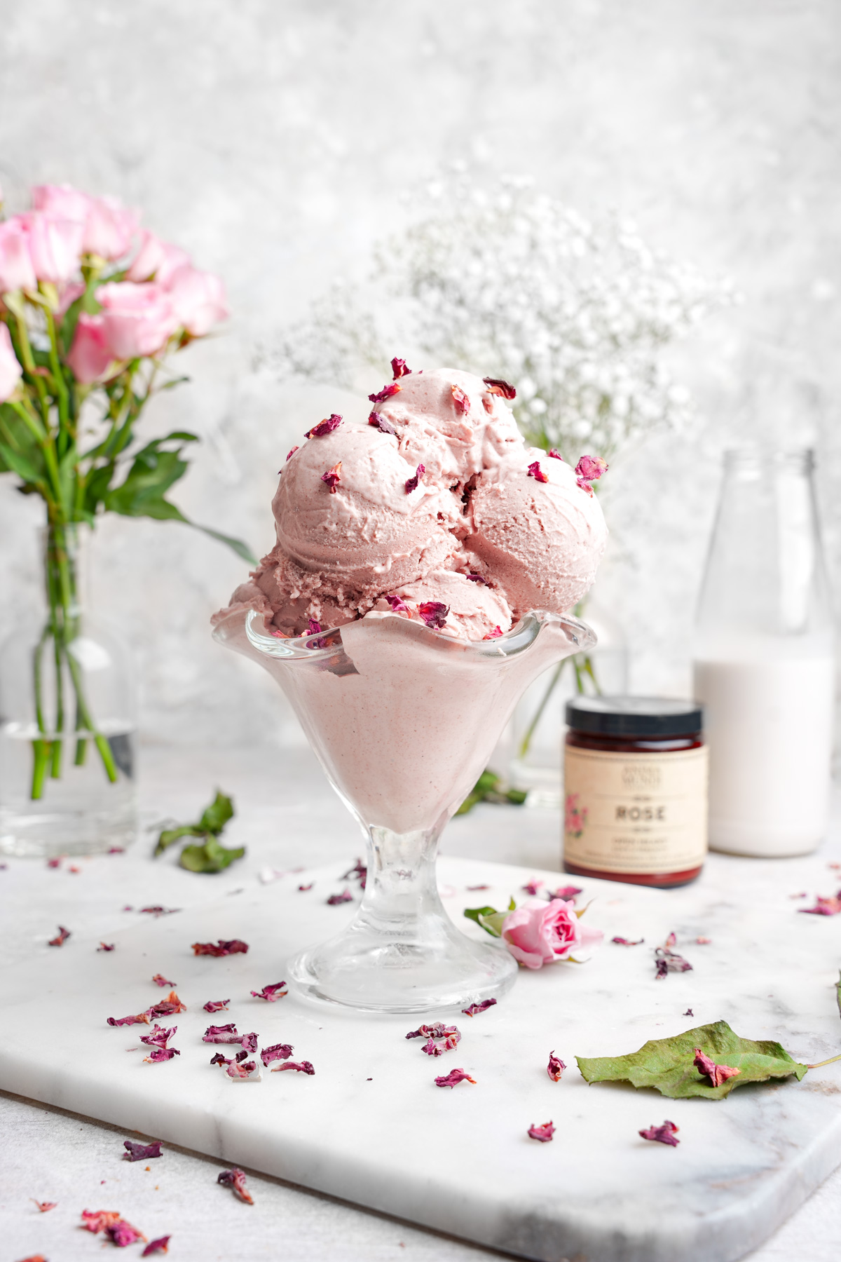 the rose ice cream in an ice cream serving bowl with fresh rose petals and roses around it