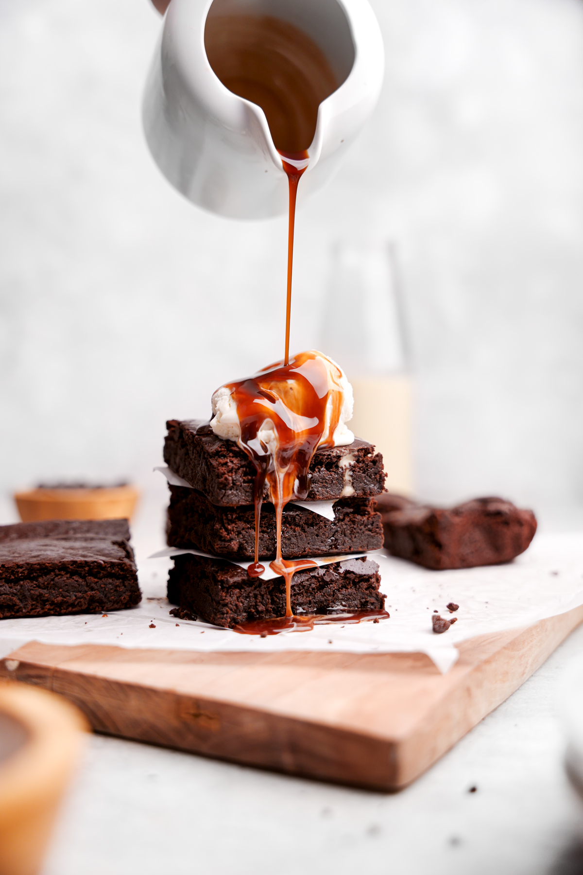 pouring chocolate sauce over a stack of the nut-free brownies with vanilla ice cream