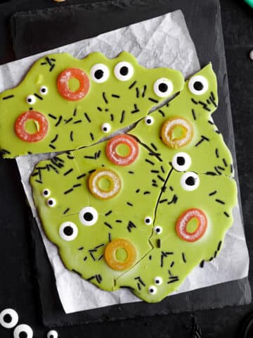 Bright green vegan Halloween candy bark topped with candy eyeballs, orange gummy rings, and black sprinkles, broken into fun pieces.
