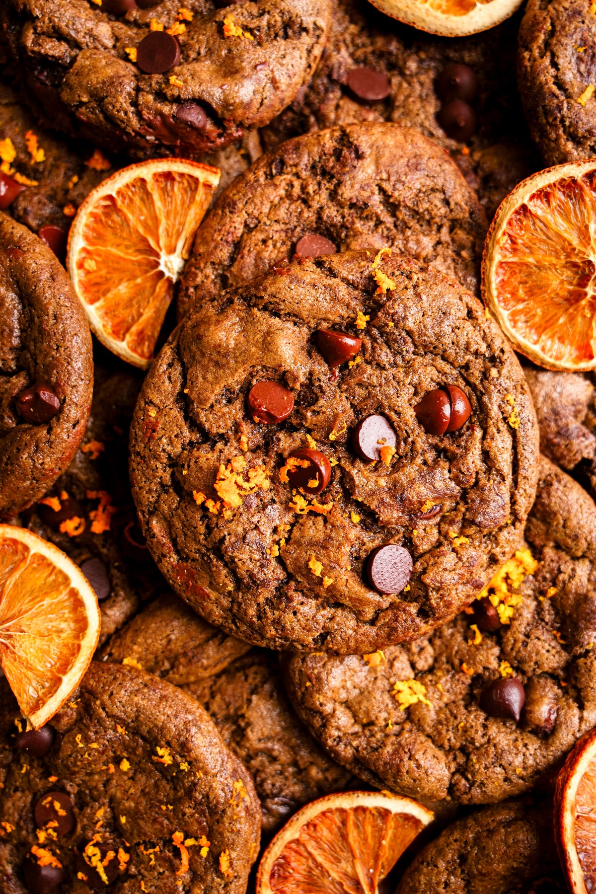 the chocolate orange cookies stacked on top of each other with fresh orange zest on top and dried oranges around it