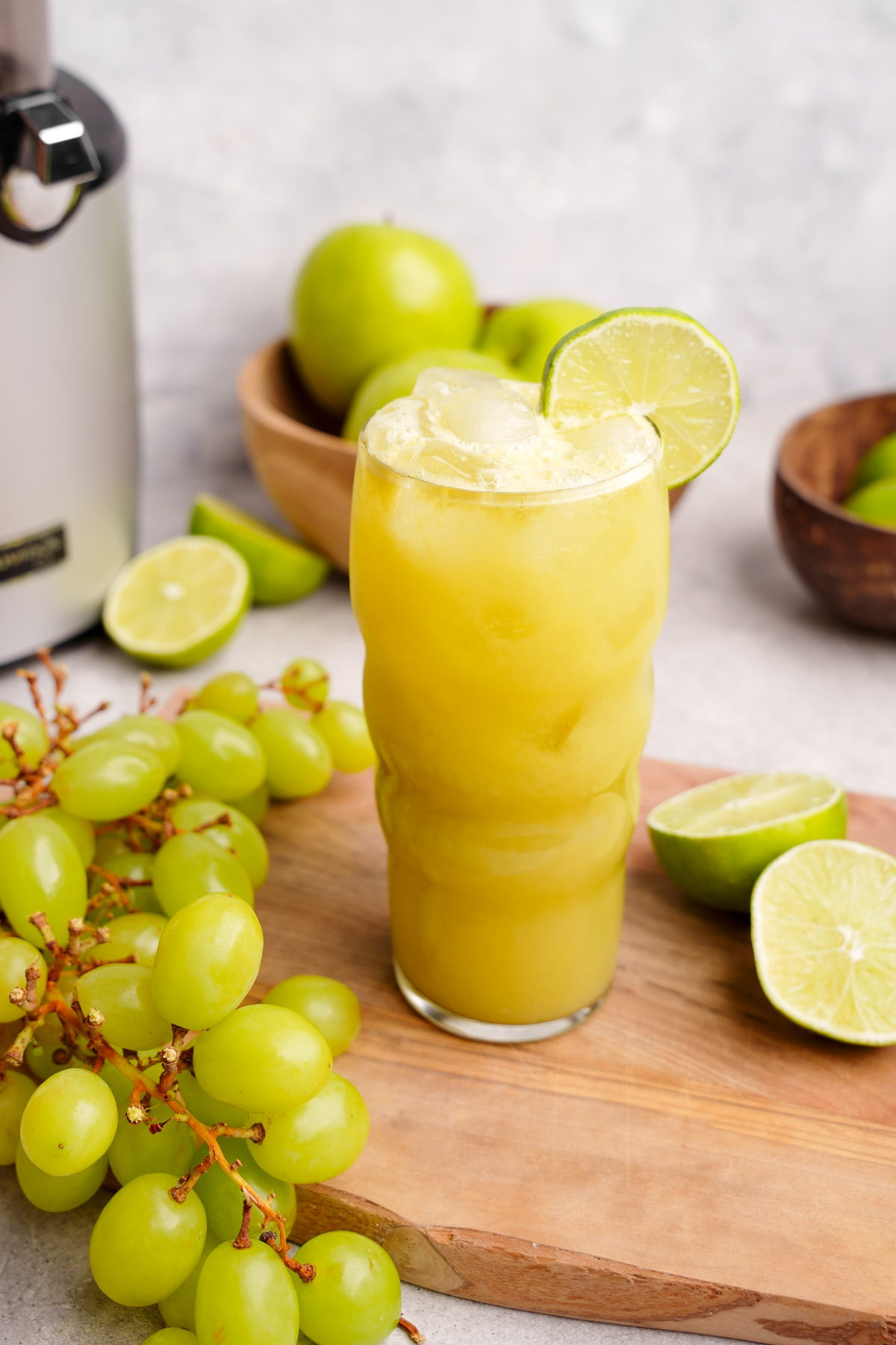 a close up of the green grape juice recipe with fresh grapes and limes all around it