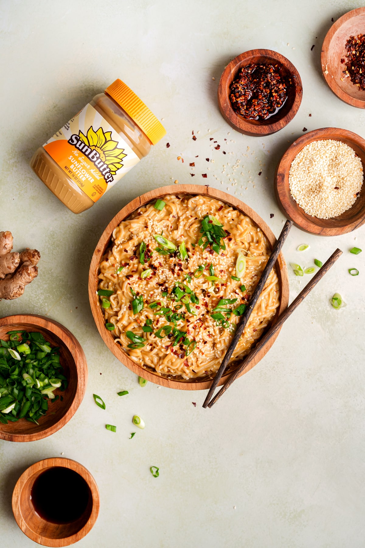 looking down at the spicy sesame noodles with the sun butter container and small bowls filled with garnishes around the noodles