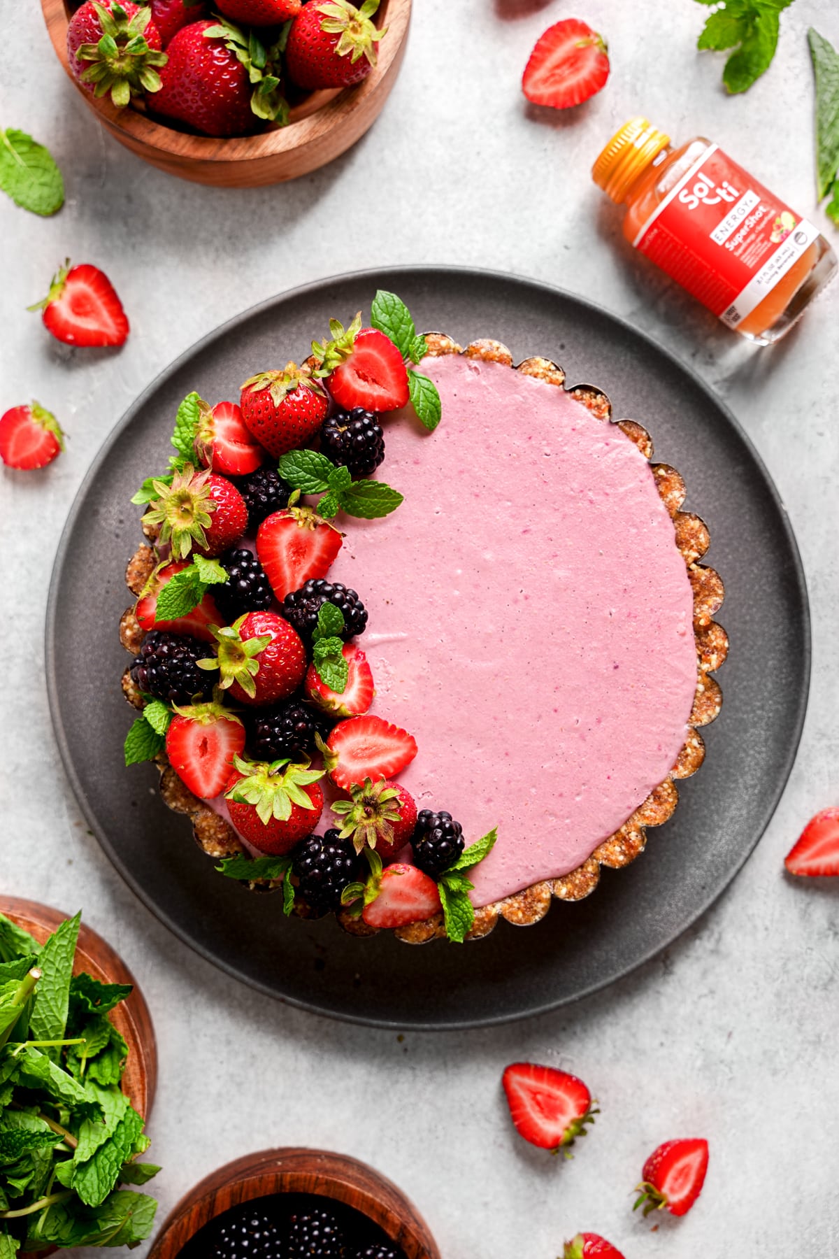 looking down at the raw vegan berry tart with fresh berries garnished on top and the sol-ti energy supershot next to it