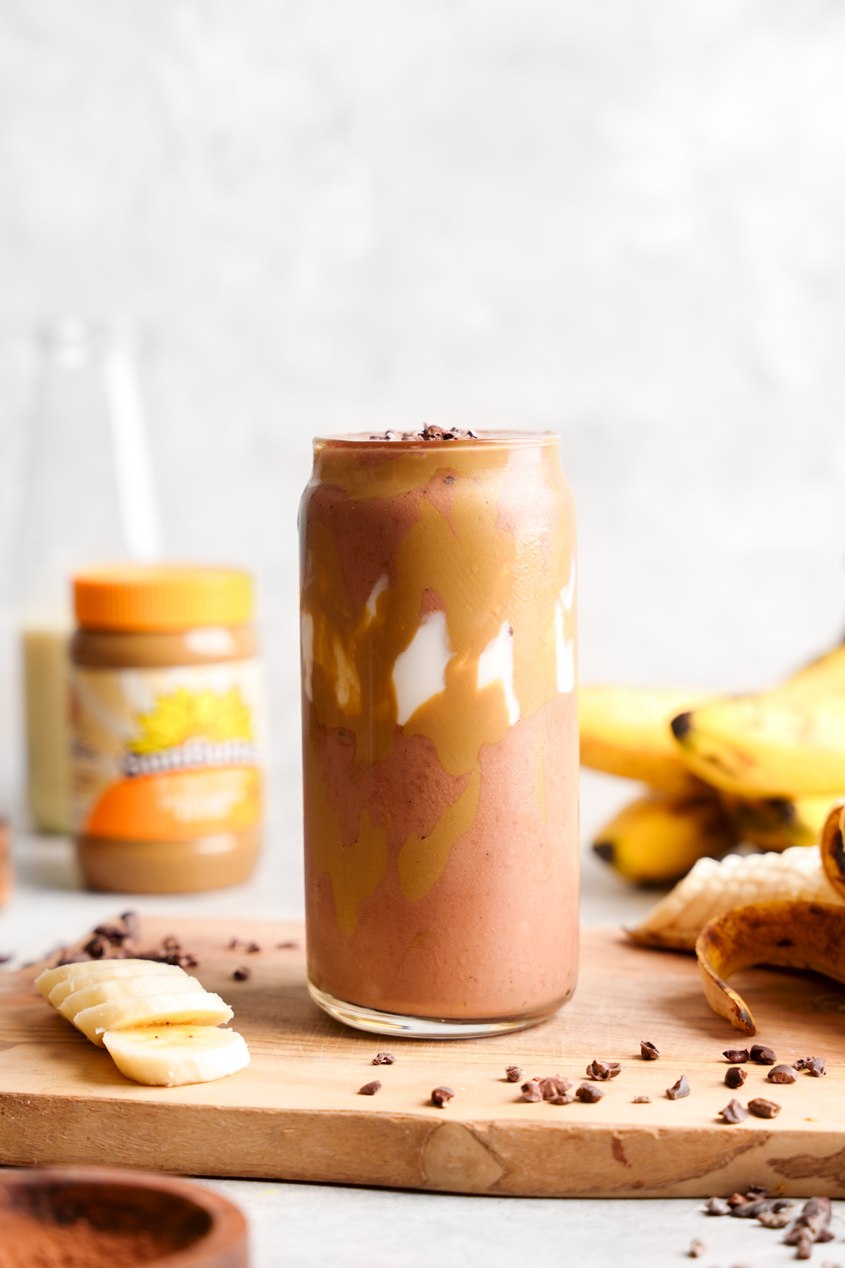the chocolate banana smoothie in a tall glass with the sunbutter no sugar added sunflower seed butter next to it