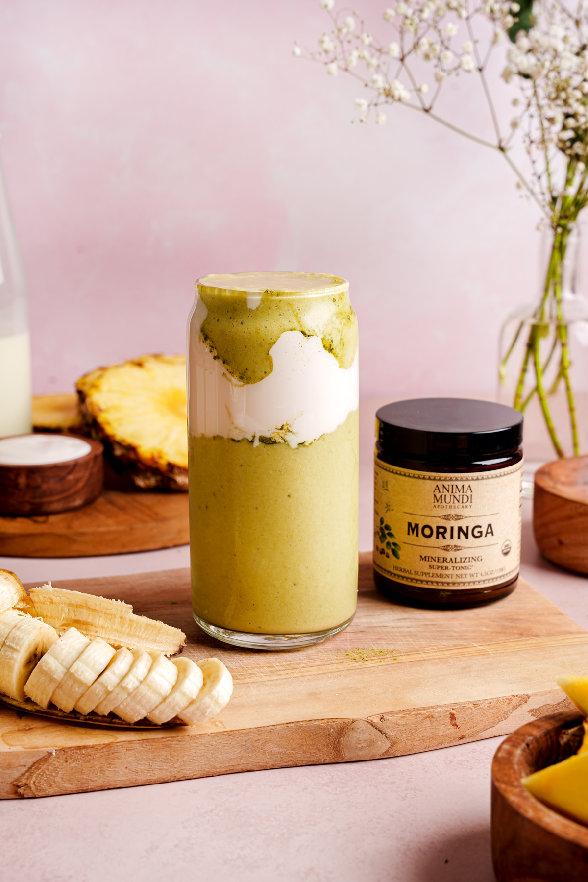the moringa smoothie next to the anima mundi container and fresh fruit around it