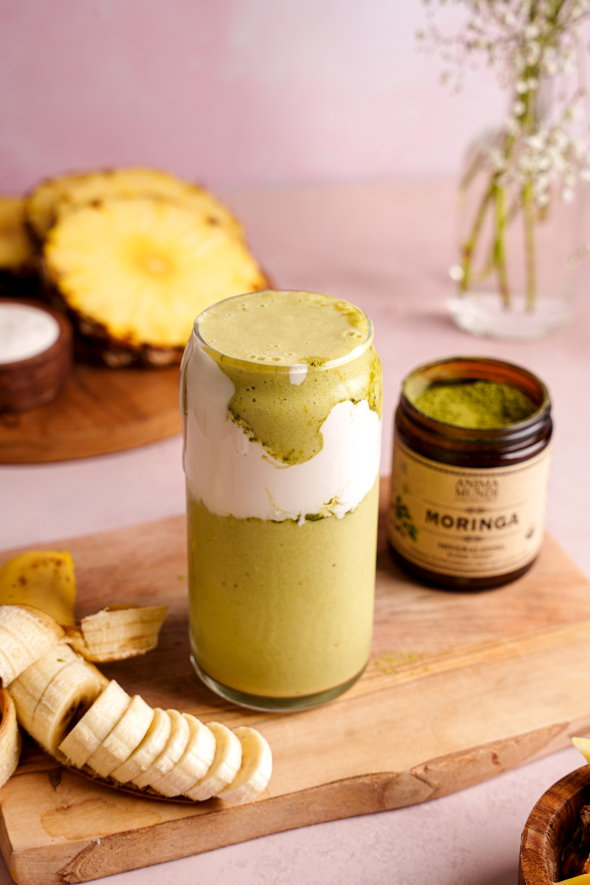 the moringa smoothie with an open container of the anima mundi moringa powder to show the bright green color
