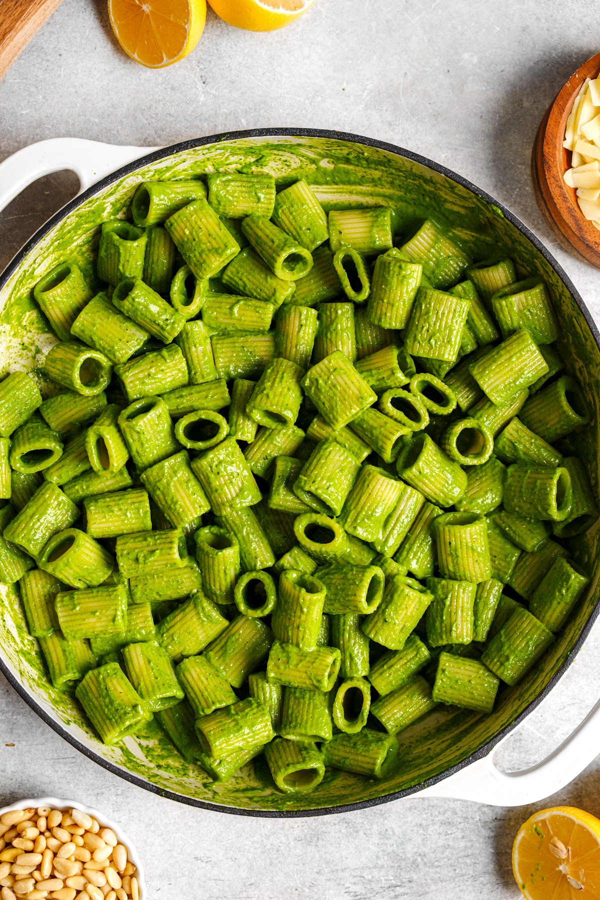 the spinach pesto pasta in a casserole dish with pine nuts and lemons next to it