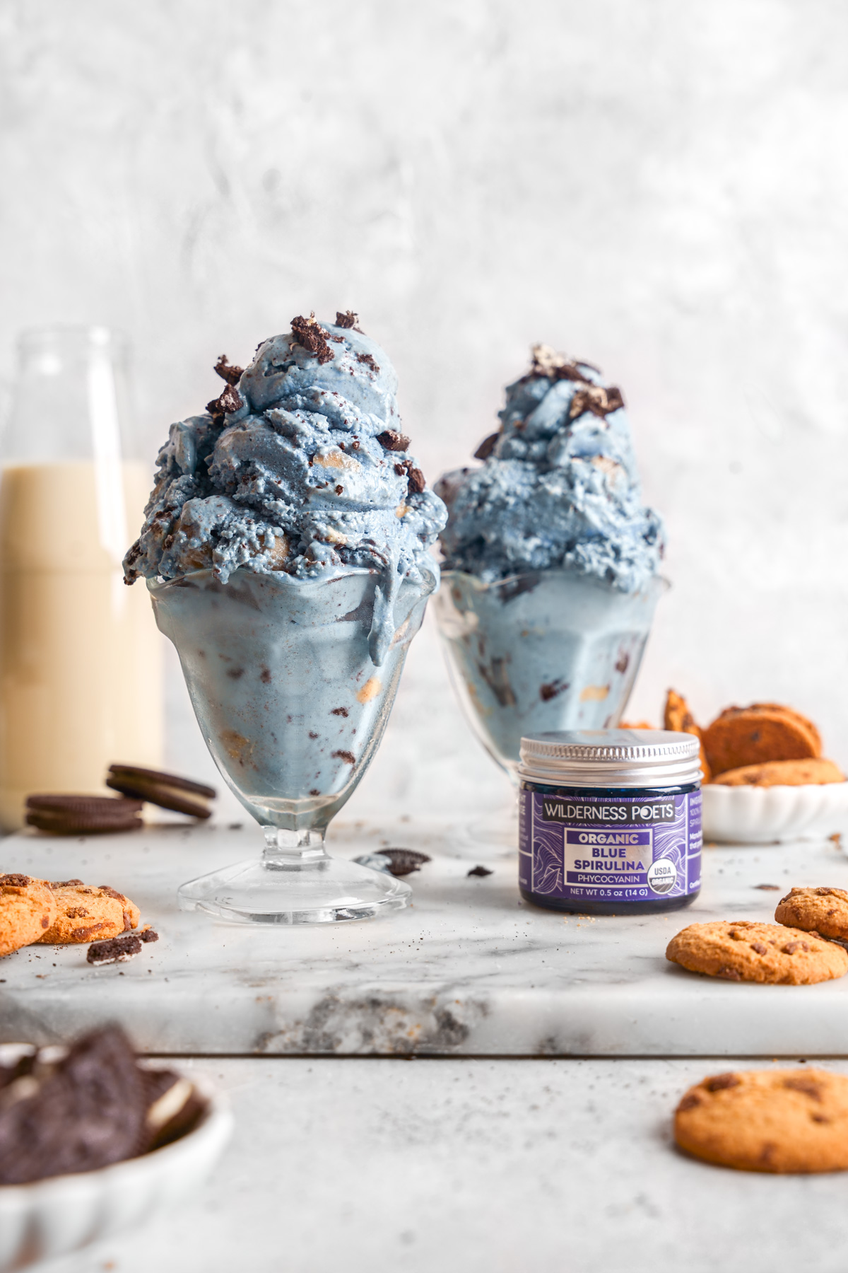 the cookie monster ice cream scooped into glasses with the wilderness poets blue spirulina next to it
