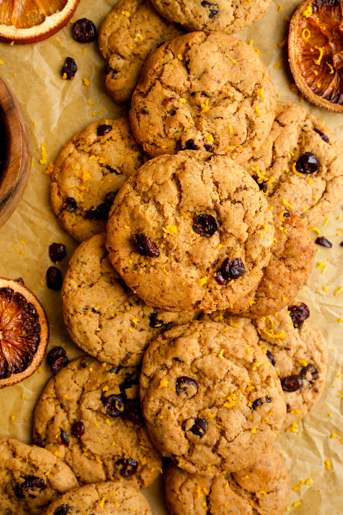 looking down at the vegan cranberry orange cookies stacked on top of each other with oranges and cranberries all around