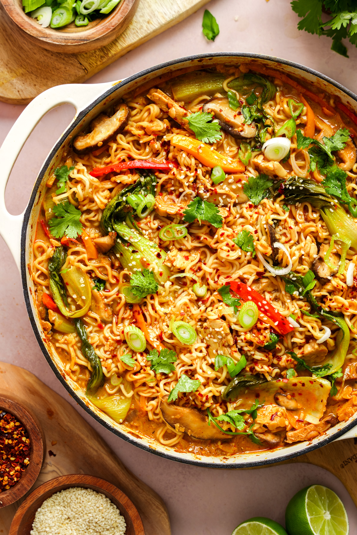 a close up of the vegan ramen in a pot with limes and spices around it