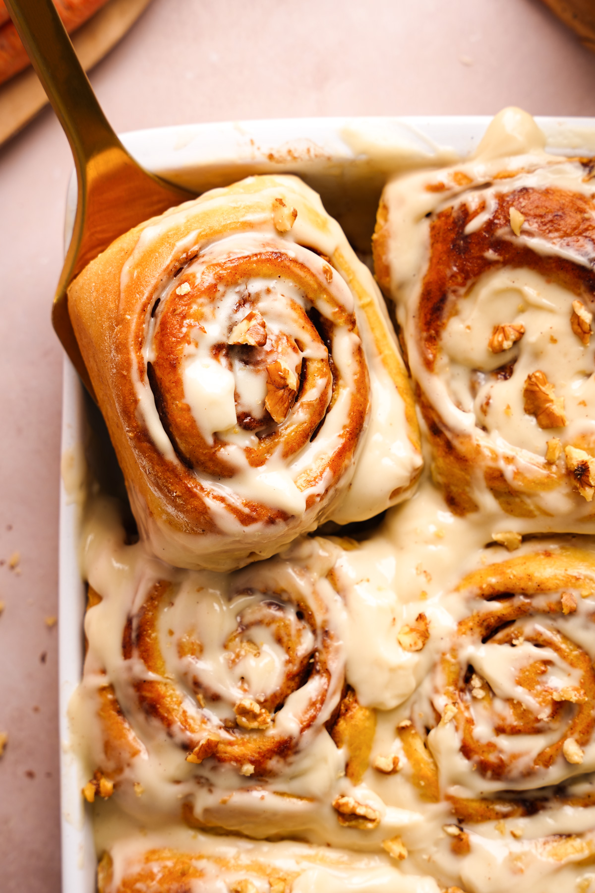 one of the carrot cake cinnamon rolls being removed from the pan