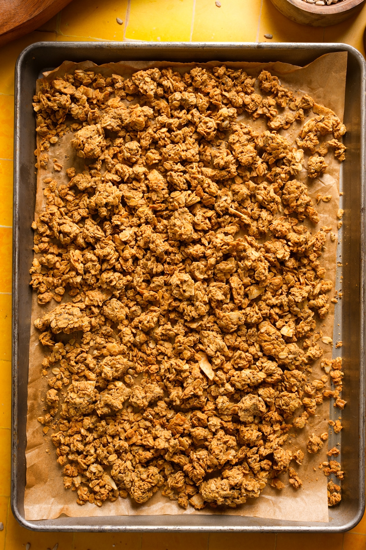 Freshly baked high protein granola with oats, sunflower seeds, and shredded coconut, spread on a parchment-lined baking sheet with golden clusters and crisp texture.