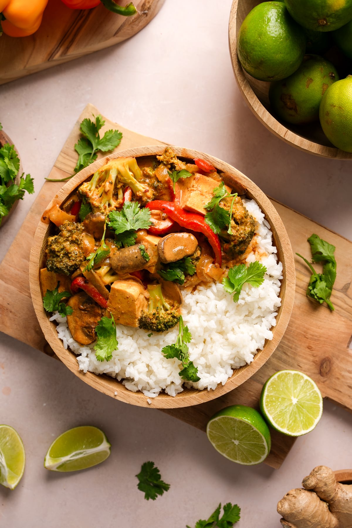 Nut-free vegan tofu Panang curry served with steamed white rice in a wooden bowl, garnished with fresh cilantro and lime wedges, featuring broccoli, mushrooms, and red bell peppers in a creamy coconut curry sauce.