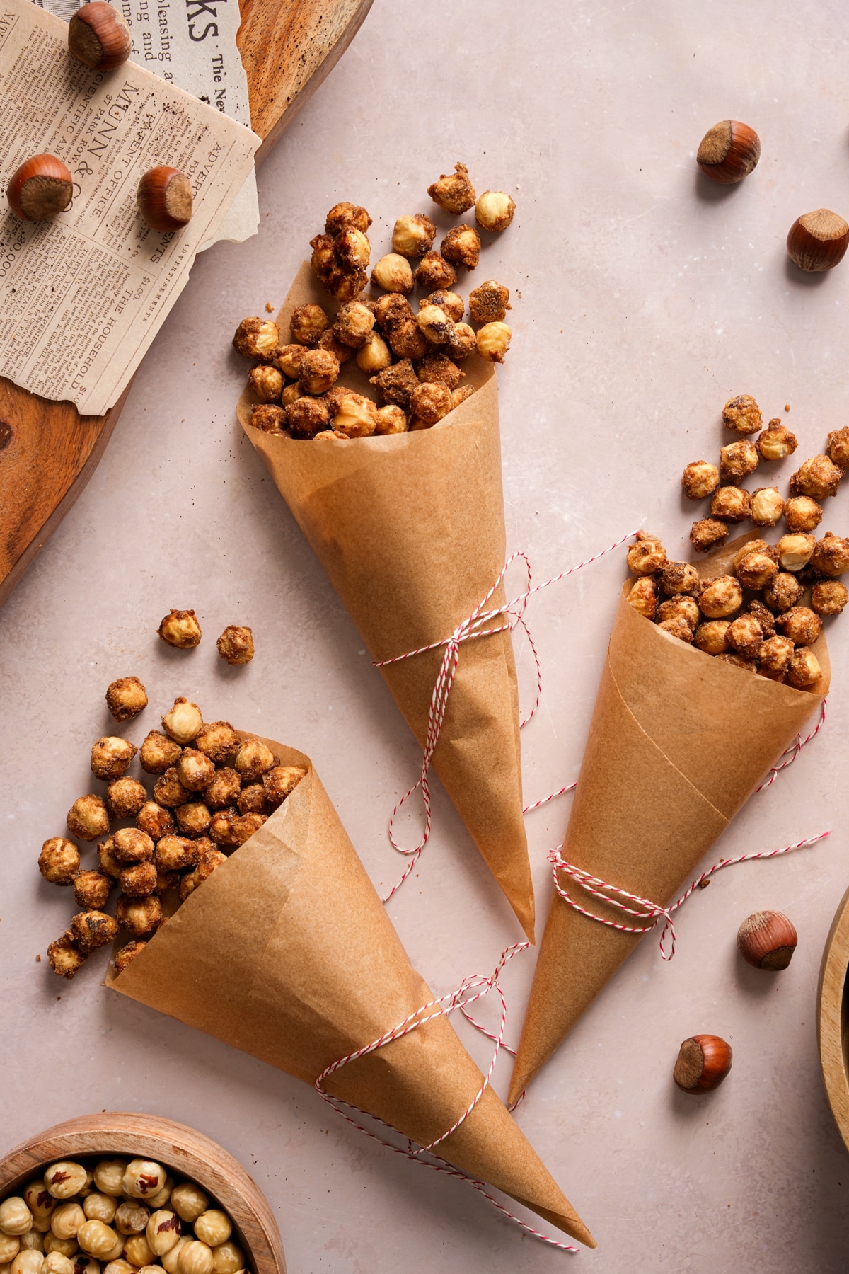 Homemade candied hazelnuts served in brown paper cones tied with red and white string on a neutral background