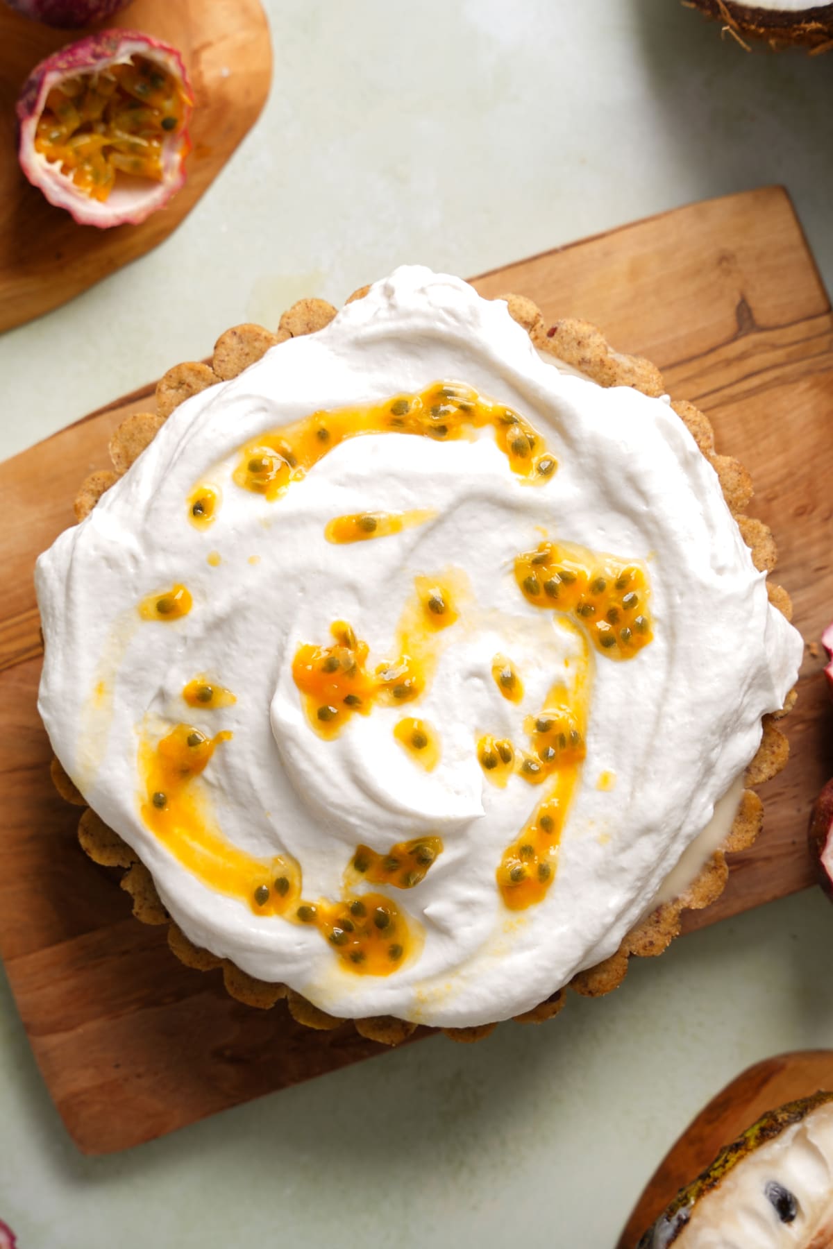 Homemade vegan soursop pie with a coconut cream topping and fresh passion fruit drizzle, displayed overhead on a wooden board