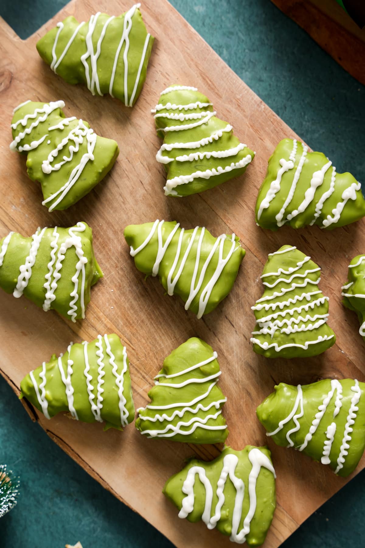 Assortment of matcha-coated Christmas tree treats on a wooden board, each decorated with unique white chocolate drizzle patterns