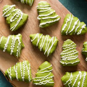 Assorted green chocolate Christmas tree treats decorated with white drizzle, arranged on a wooden serving board for a healthy holiday dessert.