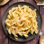 A top view of a plate of creamy vegan truffle pasta topped with dairy-free parmesan and microgreens, served on a dark plate over a rustic wooden table.