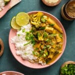 Bowl of vegan yellow curry served with fluffy white rice, tofu, broccoli, baby corn, and vegetables in a creamy coconut curry sauce, garnished with fresh cilantro, sesame seeds, and lime wedges.