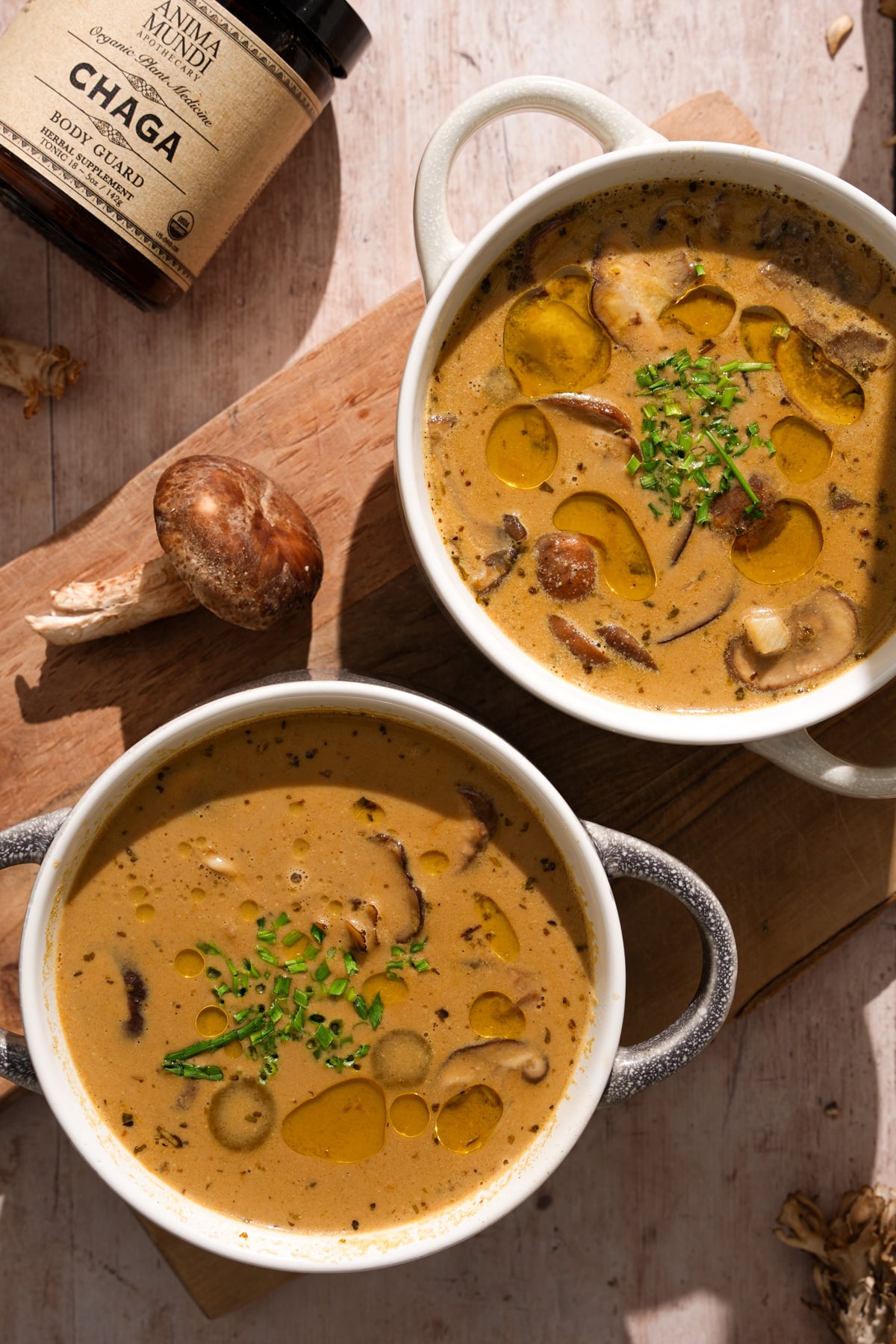 Creamy vegan mushroom soup made with chaga mushrooms, served in ceramic mugs and topped with olive oil and fresh chives - healthy dairy-free mushroom soup recipe with medicinal mushrooms and herbs.