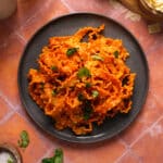 Overhead view of mafaldine pasta coated in a creamy dairy-free vodka sauce, garnished with fresh basil and served in a dark bowl on a warm terracotta surface.