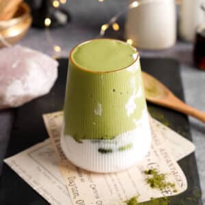 Green liver detox smoothie made with herbal liver greens layered over creamy plant milk in a ribbed glass, styled on a slate board with wellness powders and a wooden spoon.